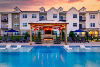 A pool area with a gazebo and lounge chairs in front of a multi-story apartment building.